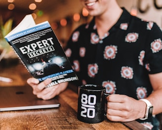 smiling man reading book while holding mug