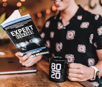 smiling man reading book while holding mug