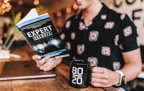 smiling man reading book while holding mug