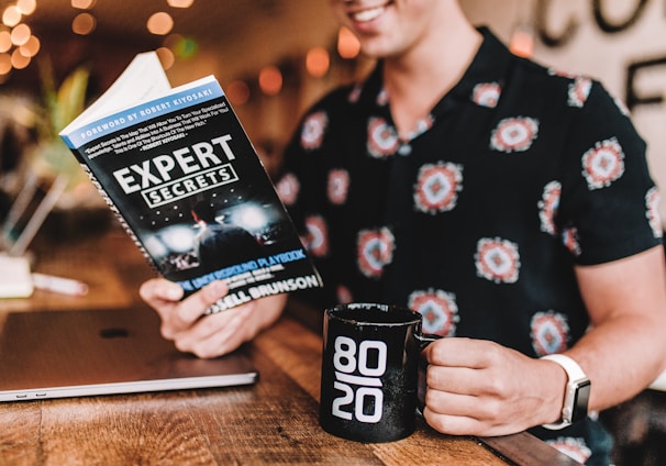 smiling man reading book while holding mug