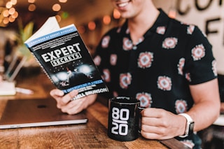 smiling man reading book while holding mug
