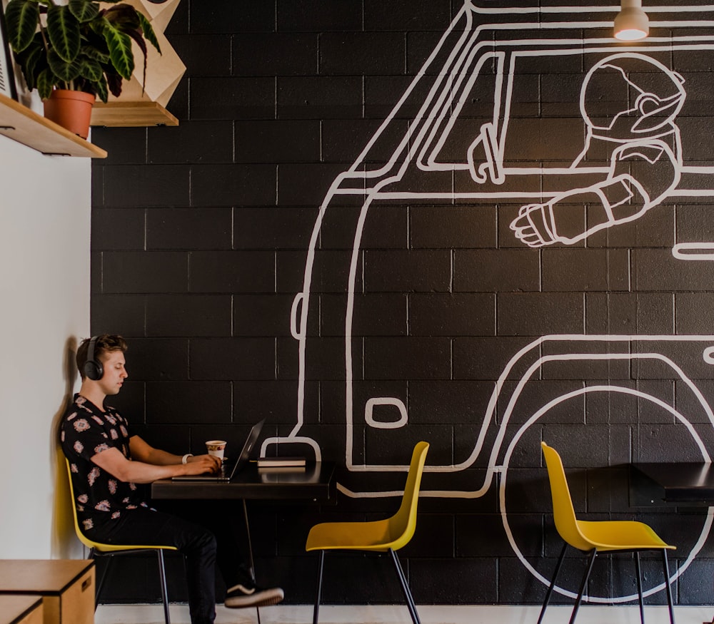 uomo che indossa la cuffia usando il computer portatile mentre è seduto accanto al tavolo all'interno del caffè