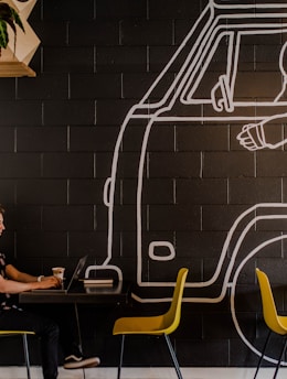 man wearing headphone using laptop while sitting beside table inside cafe