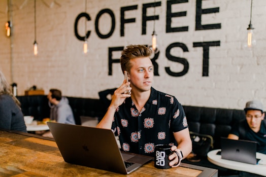 Junger Mann telefoniert in einem Café mit Laptop und Kaffeetasse – moderner Lifestyle und Business