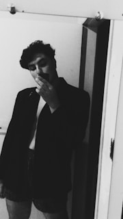 A minimalist black and white photo showing a person looking at their reflection on a sleek digital screen displaying an outfit.