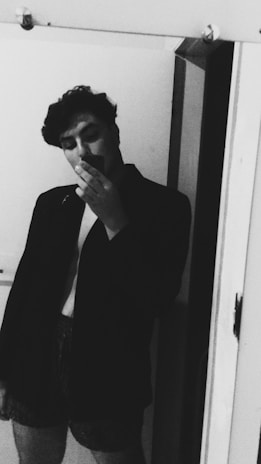 A minimalist black and white photo showing a person looking at their reflection on a sleek digital screen displaying an outfit.