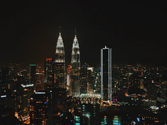 Nighttime city skyline of Kuala Lumpur with vibrant lights and towering skyscrapers.