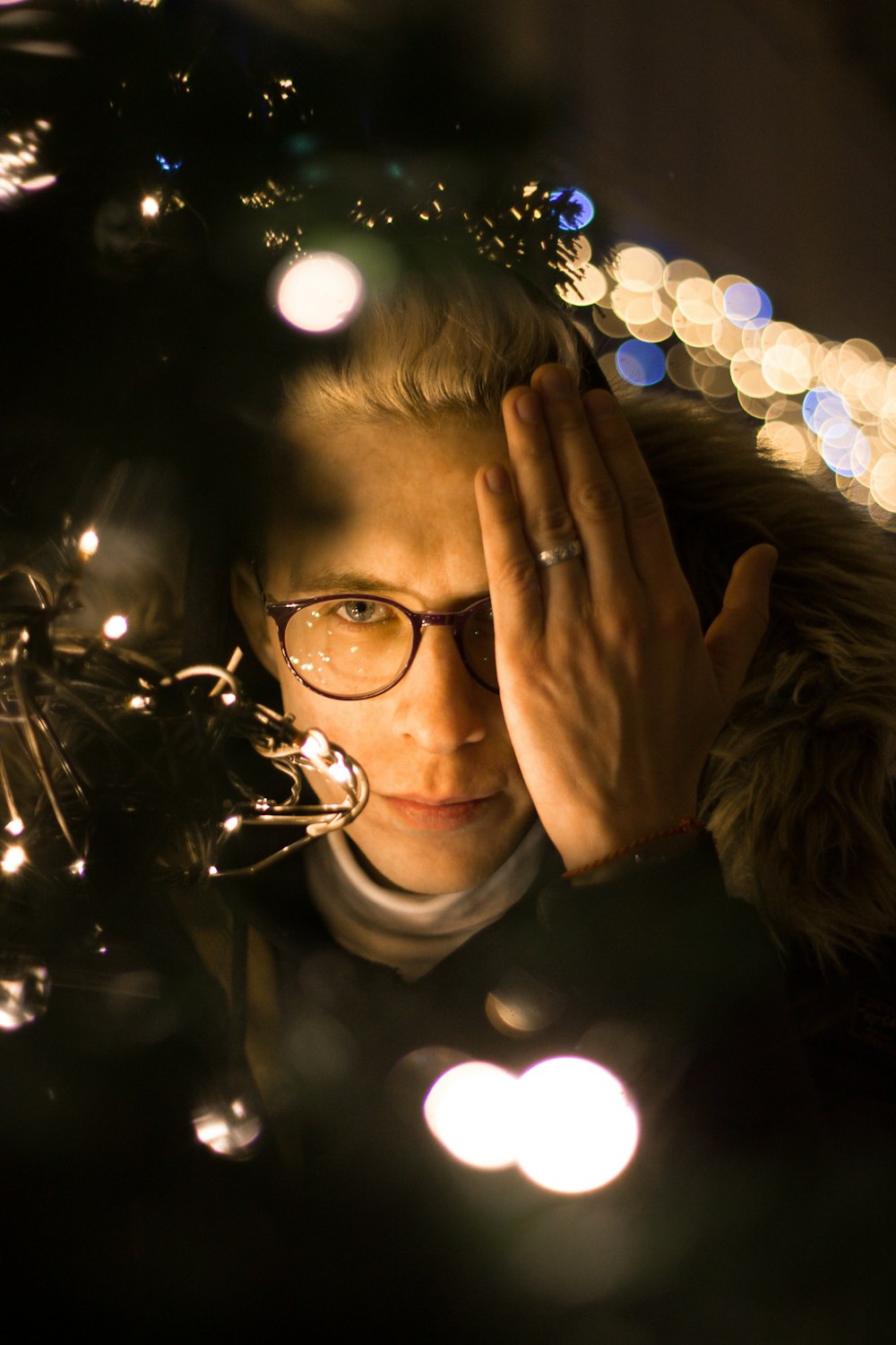 man covering his left eye standing beside pre-lit tree