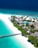 A tropical island resort featuring white sandy beaches and turquoise waters. Palm trees line the shore, and a wooden pier extends into the ocean. Thatched-roof bungalows are nestled among lush greenery, with a clear blue swimming pool visible near the center of the image.