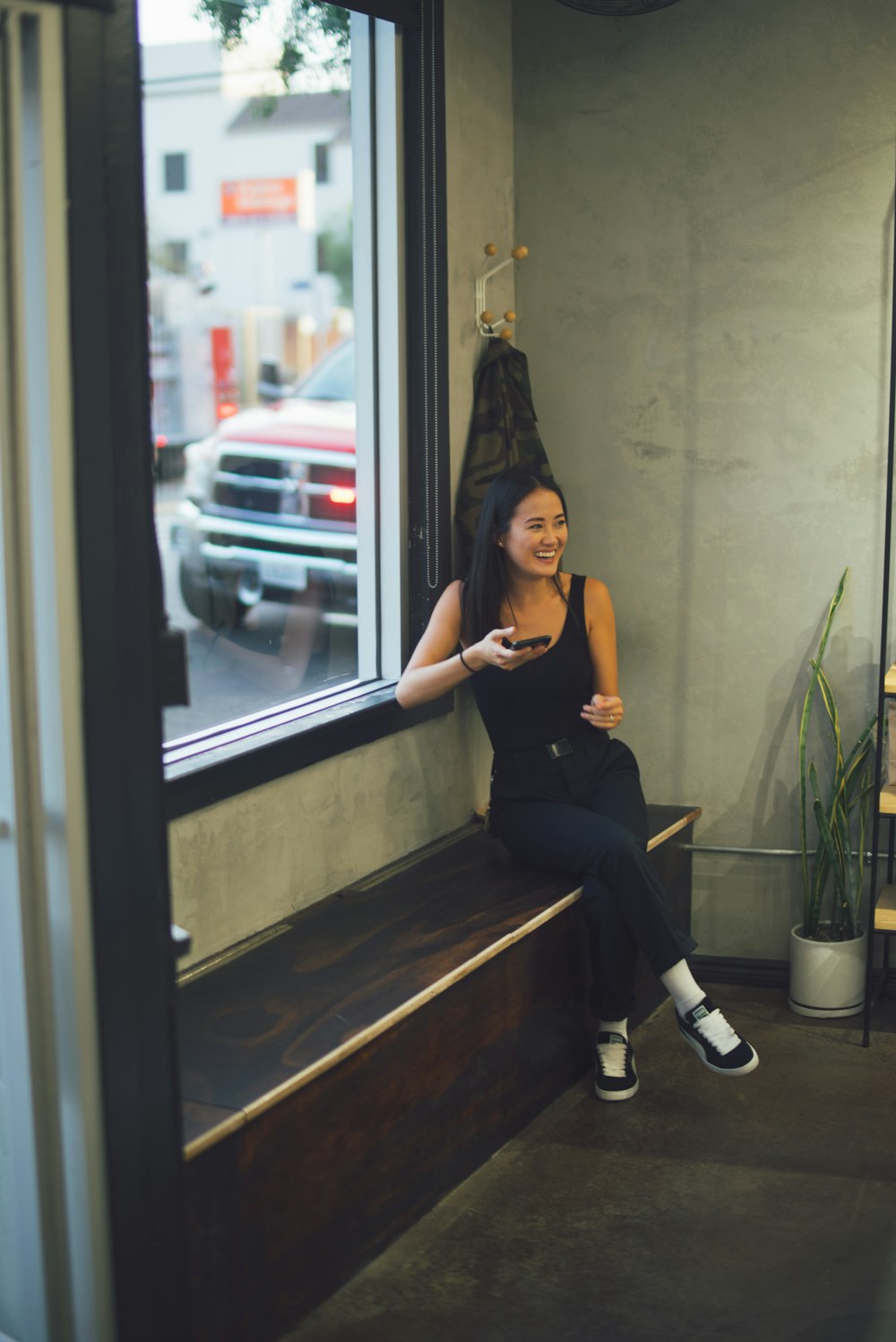 woman in black tank top sitting beside window using smartphone