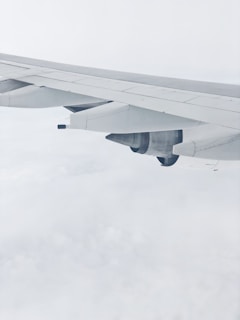 An airplane wing and engine photographed from a window seat, surrounded by a bright and cloudy sky.