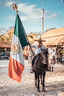 man riding on horse while holding flag of Mexico