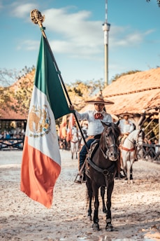 man riding on horse while holding flag of Mexico