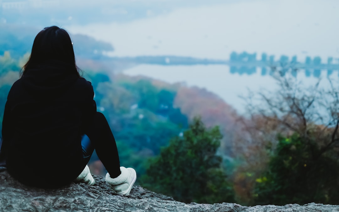 person sitting on gray rock watching sea during daytime