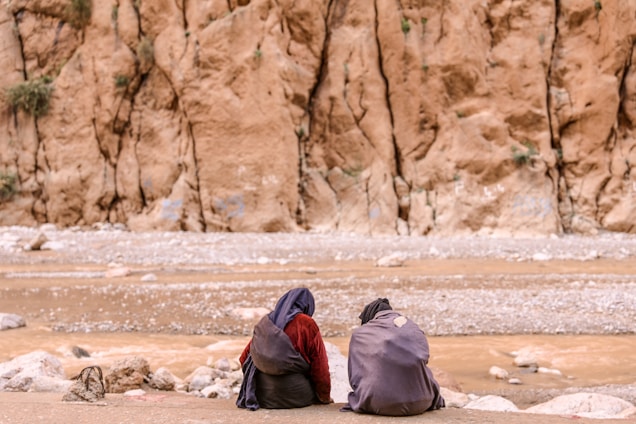 two person sitting on brown surface in front of mountain