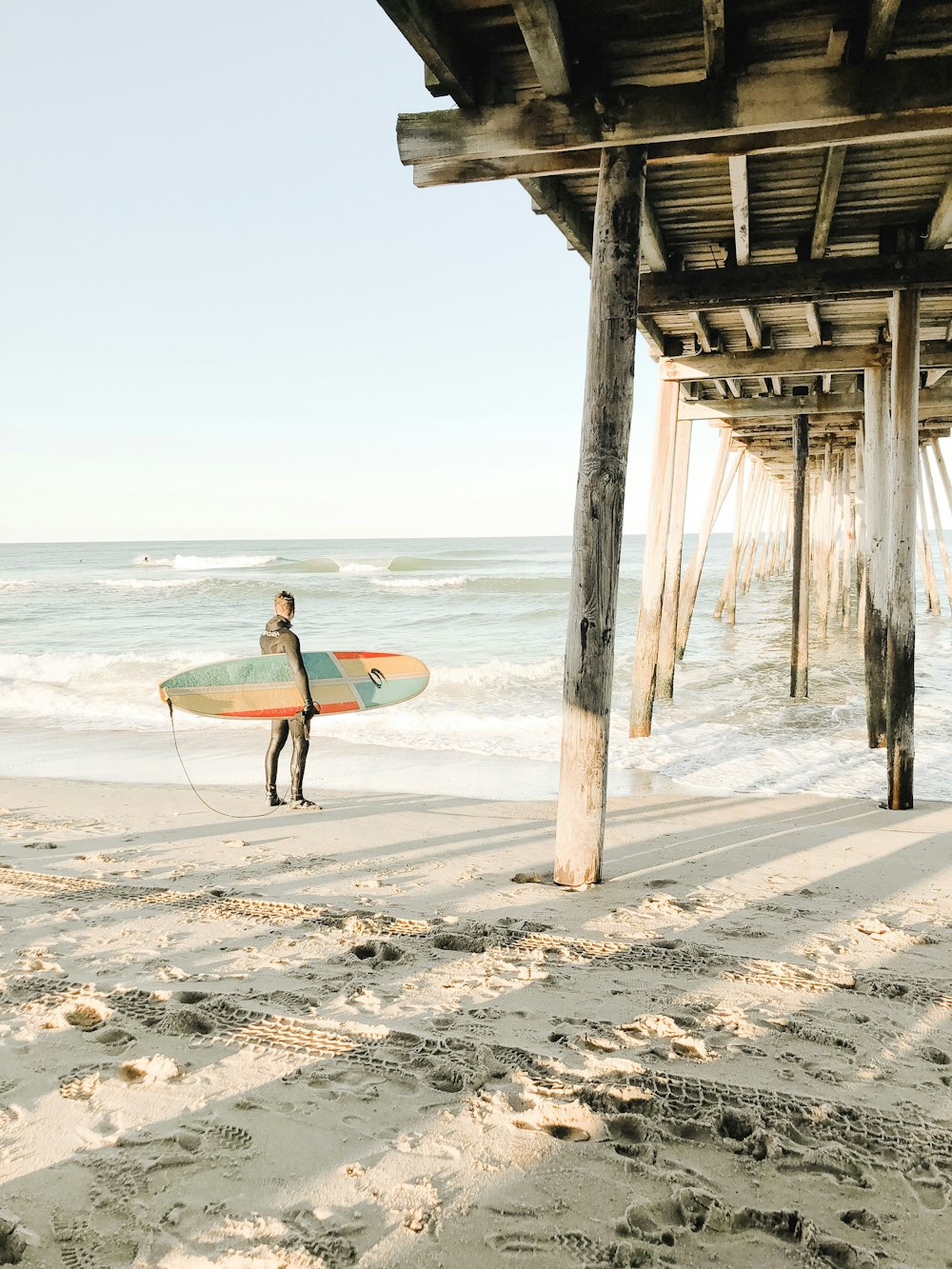 person holding surfboard while standing near brown wooden dock