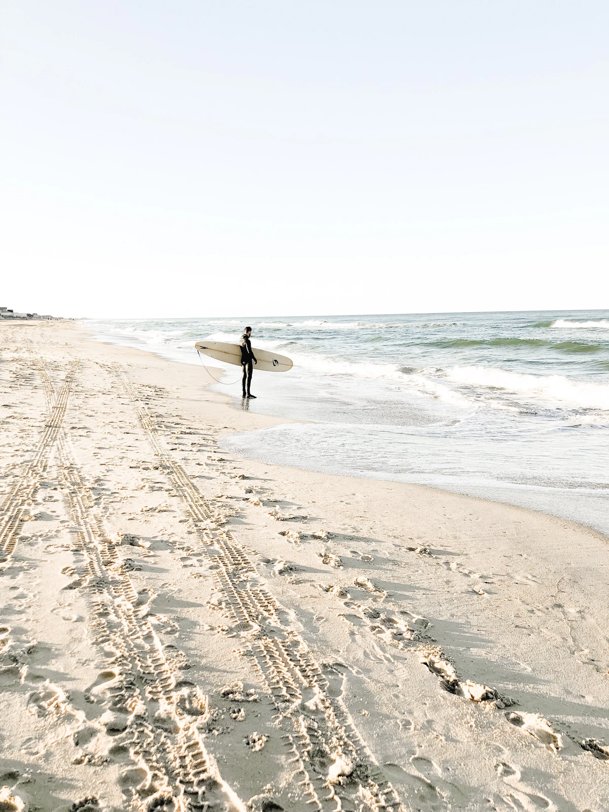 Surfer holding a surfboard on the beach. Photo by Jenna Lee on Unsplash