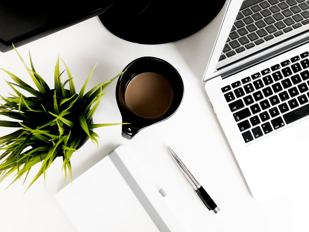 click pen beside ceramic mug and laptop on table