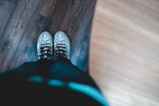 Close-up of a pair of clean, shiny sneakers on a wooden floor.