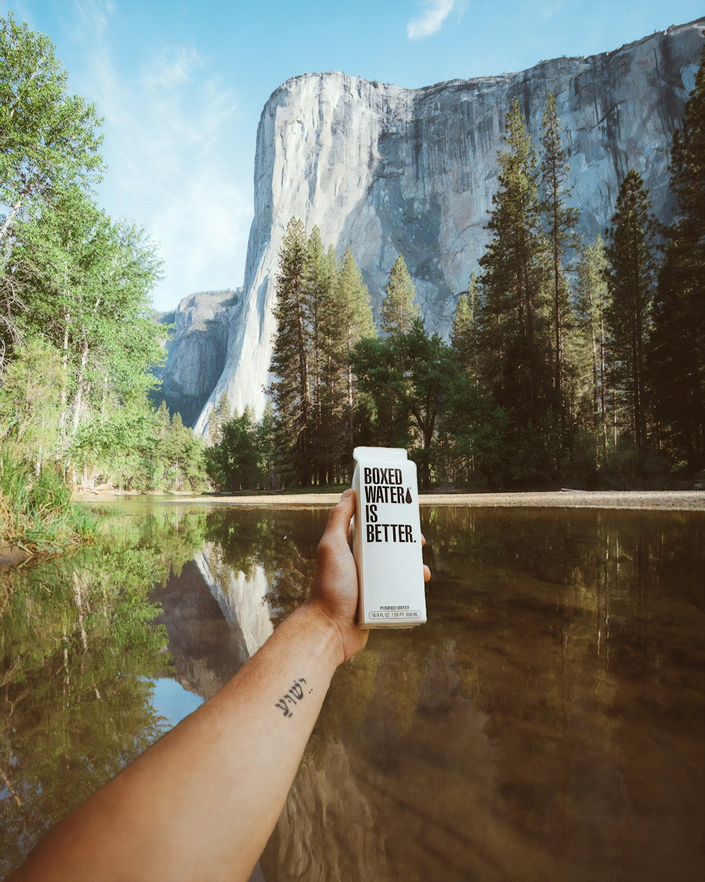 A person holding a carton of Boxed Water in their hand in front of El Capitan in Yosemite