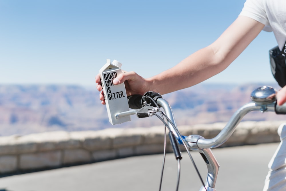 A person riding a bicycle holding Boxed Water