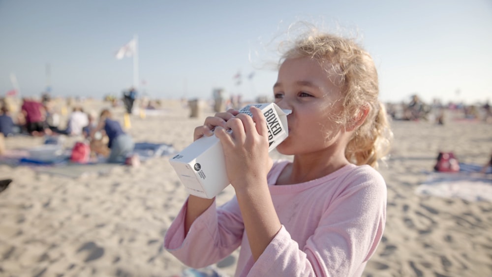 ビーチでボックスウォーターのカートンを飲む女の子