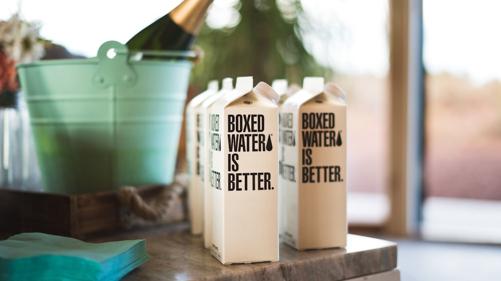 A group of Boxed Water cartons next to a green bucket