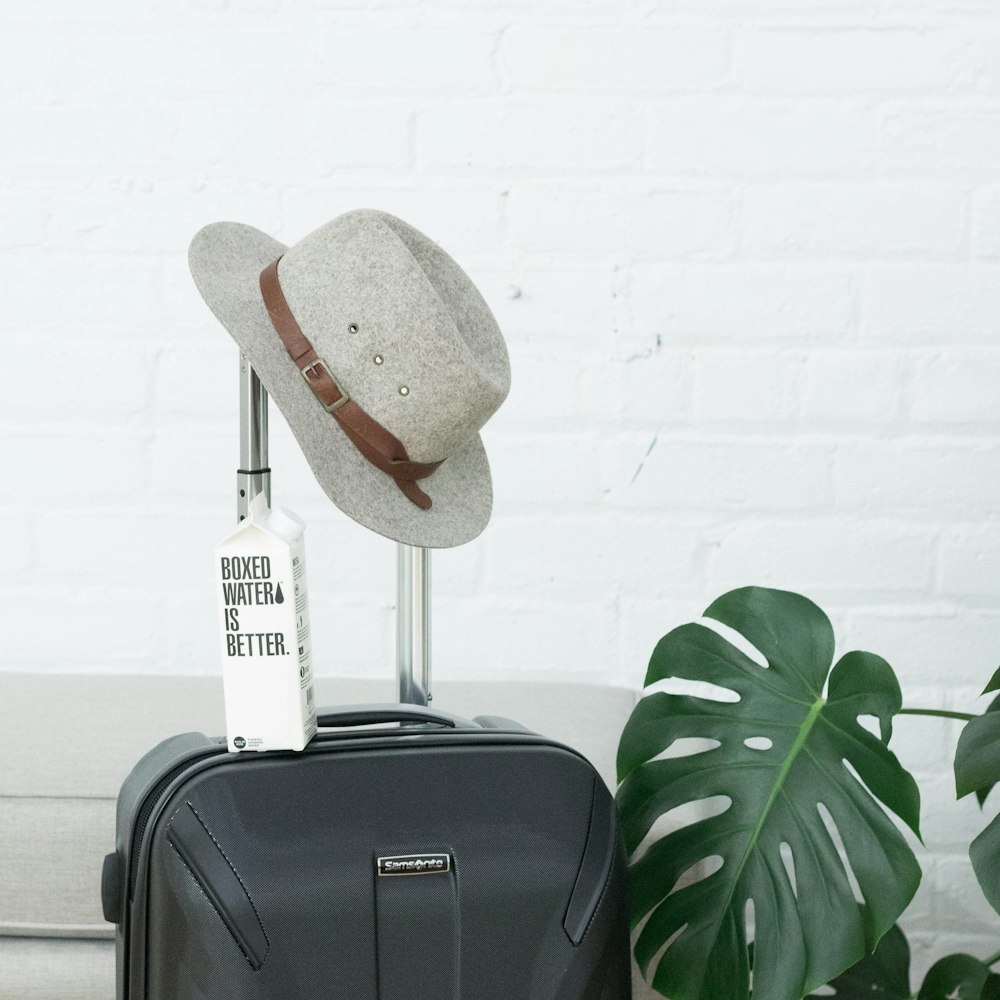 帽子と箱入りの水パックがスーツケースに載っています