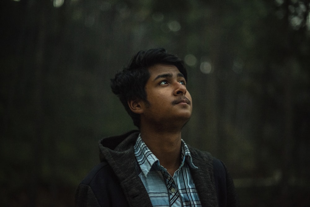 man wearing green and white collared top and black jacket staring