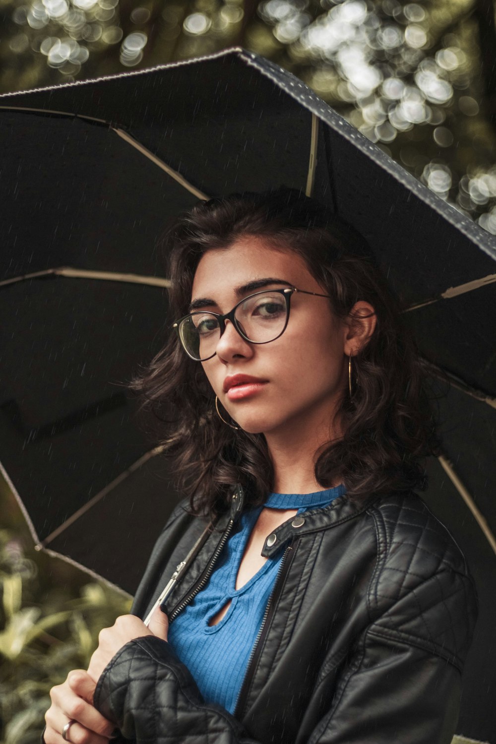 woman wearing blue crew-neck shirt and quilted black leather jacket with umbrella