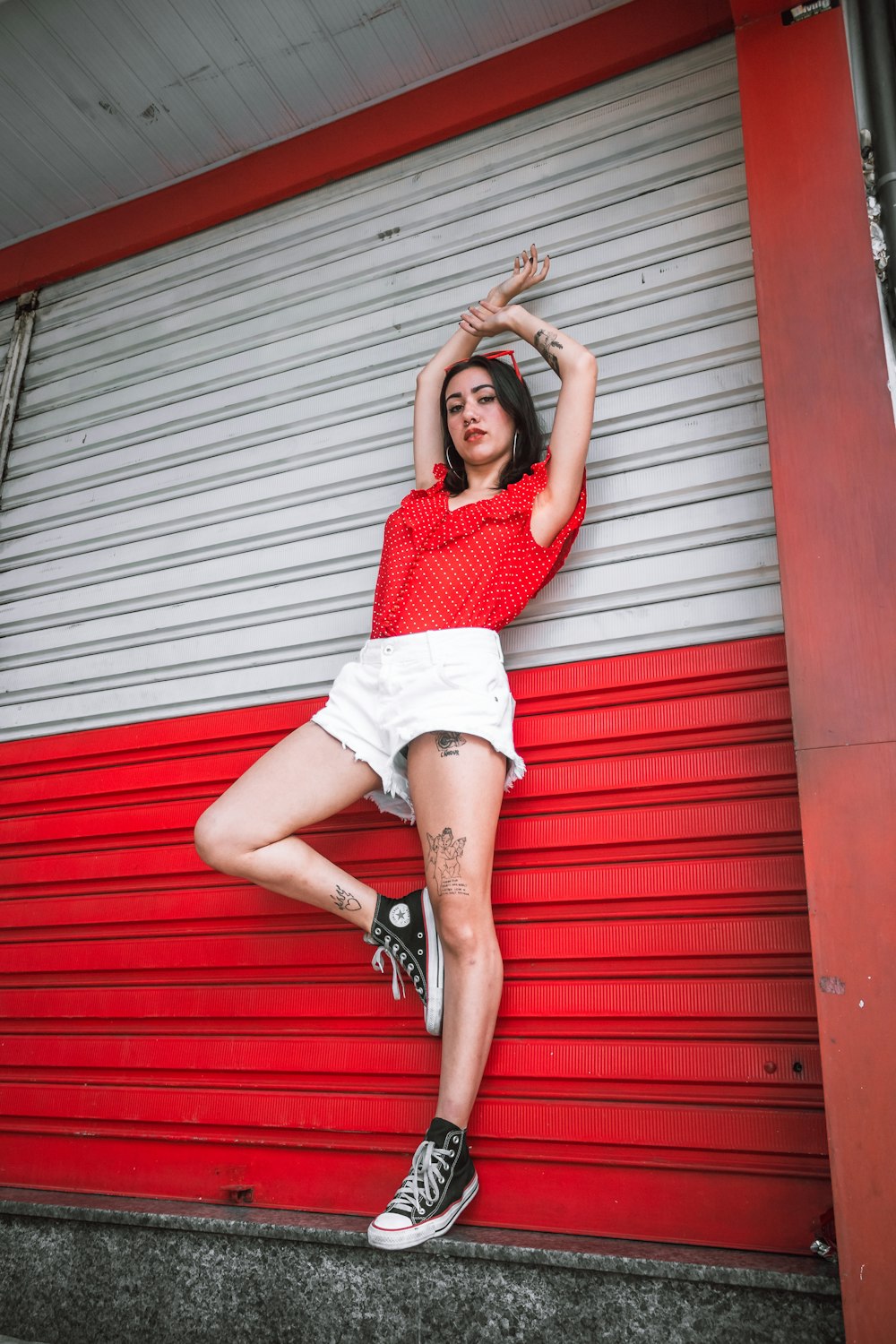 Woman wearing red sleeveless shirt and white short shorts leaning on  white-and-red roll-up door photo – Free Red Image on Unsplash