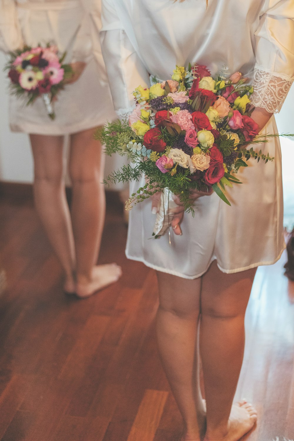 two person wearing white silk robes while holding multicolored bouquets