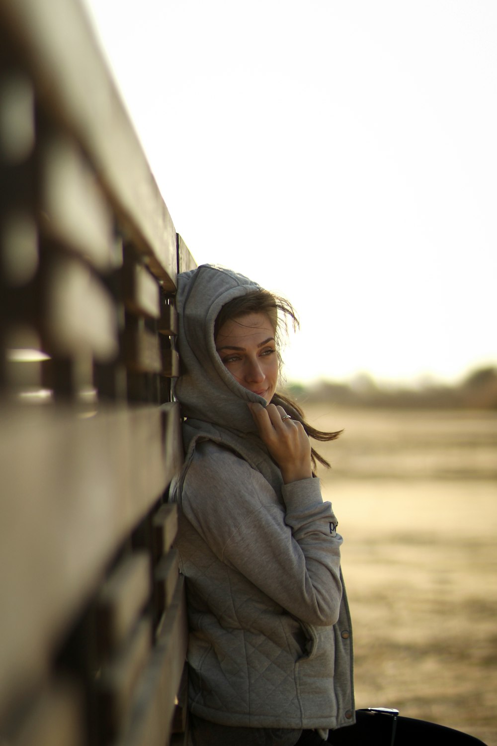 woman in gray hoodie leaning on wood
