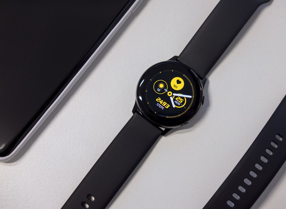 turned-on black Samsung smartwatch on white surface