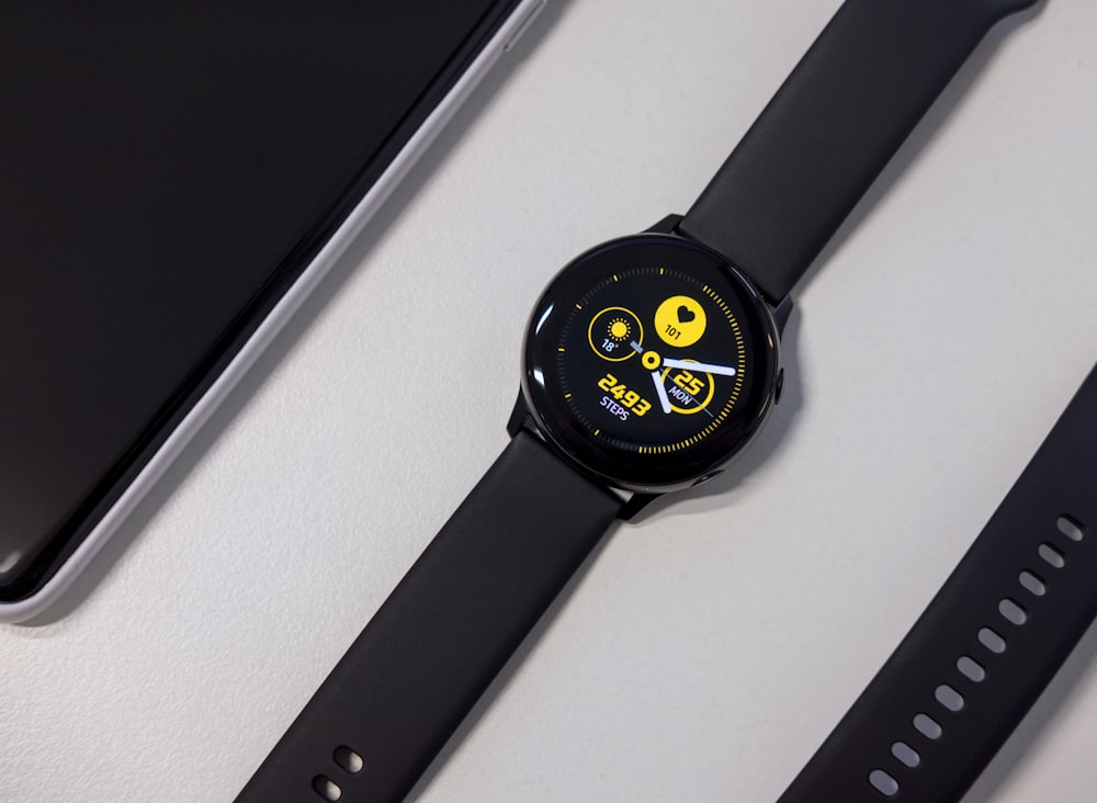 Eingeschaltete schwarze Smartwatch auf weißer Oberfläche