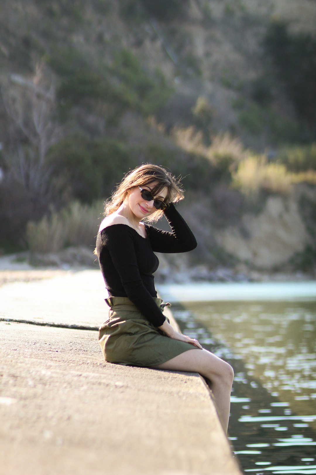 woman sitting on brown concrete surface facing body of water