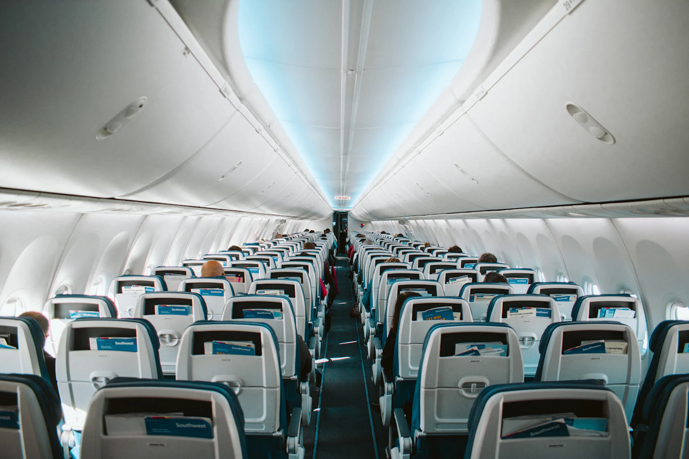 Cabina de pasajeros de un avión comercial con filas de asientos y luz azul en el techo