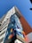 A high-rise building towers upwards with a colorful geometric mural adorning its facade. The mural features abstract shapes in vibrant blues, oranges, and yellows. The sky is clear and blue, providing a striking backdrop to the building's modern design.
