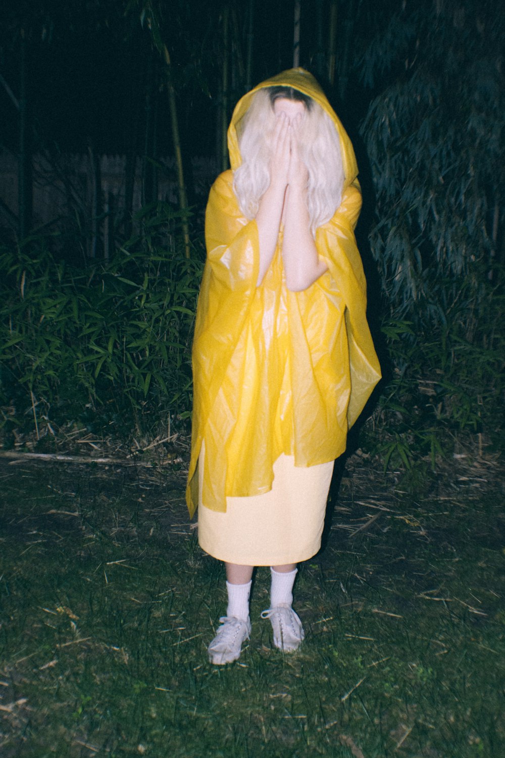 person wearing yellow raincoat covering face outdoors during nighttime