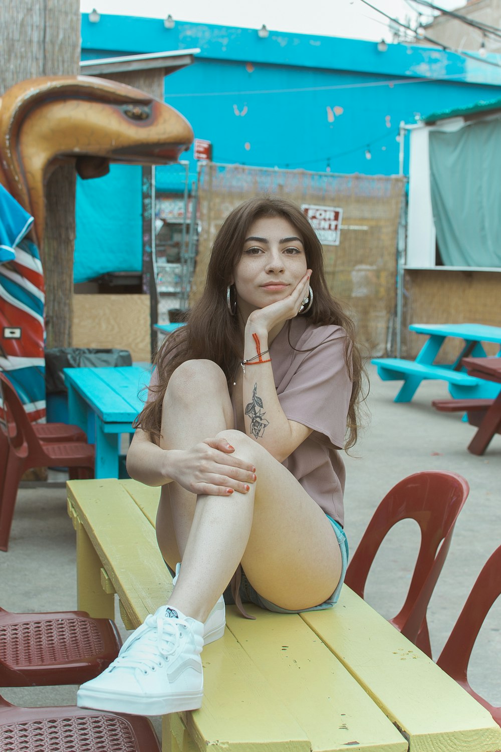 woman wearing beige screw-neck shirt and blue short sitting on yellow wooden bench