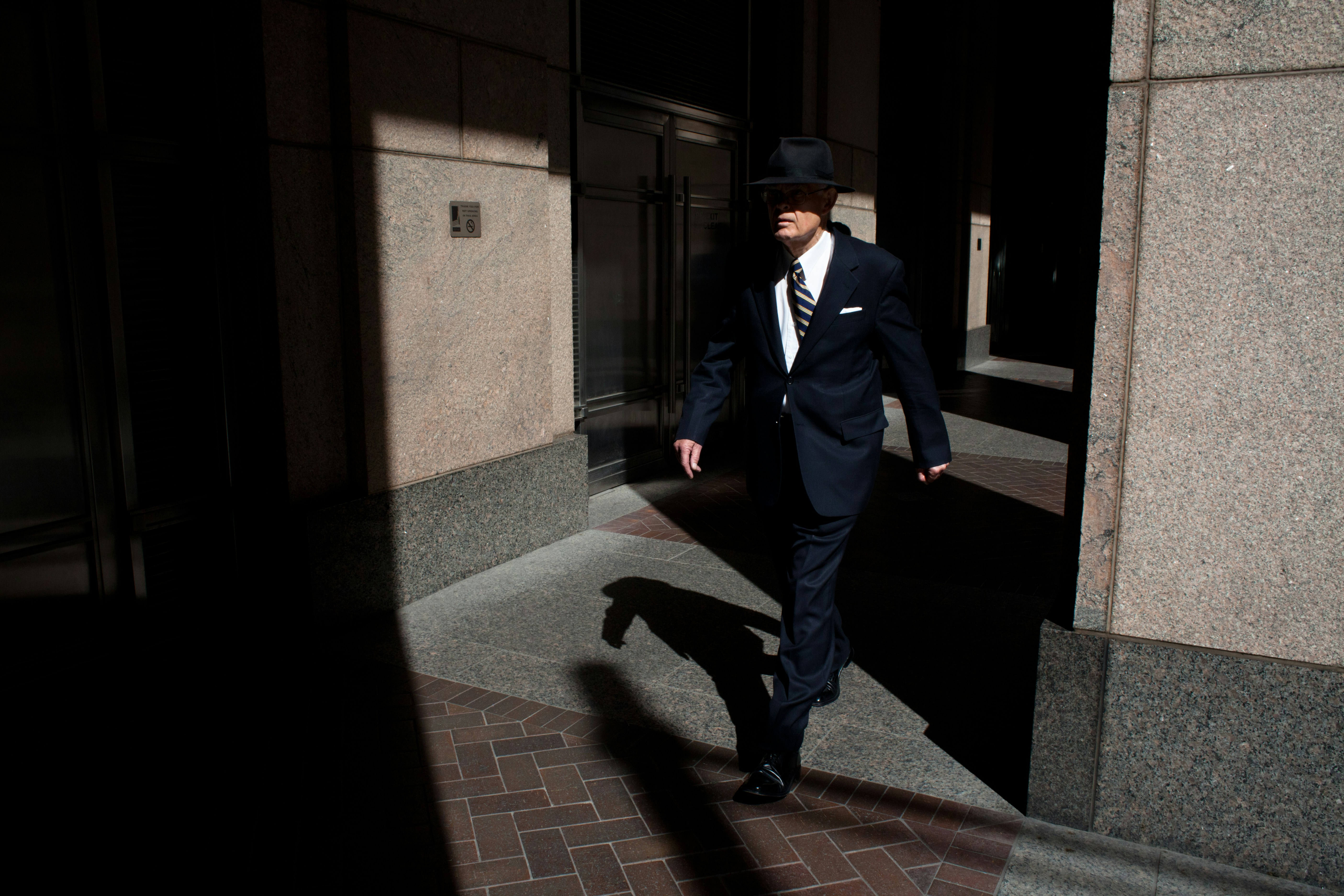 man wearing suit walking on pathway during daytime