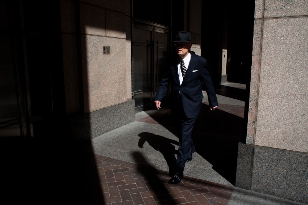 man wearing suit walking on pathway during daytime