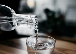 person holding bottle pouring water on drinking glass