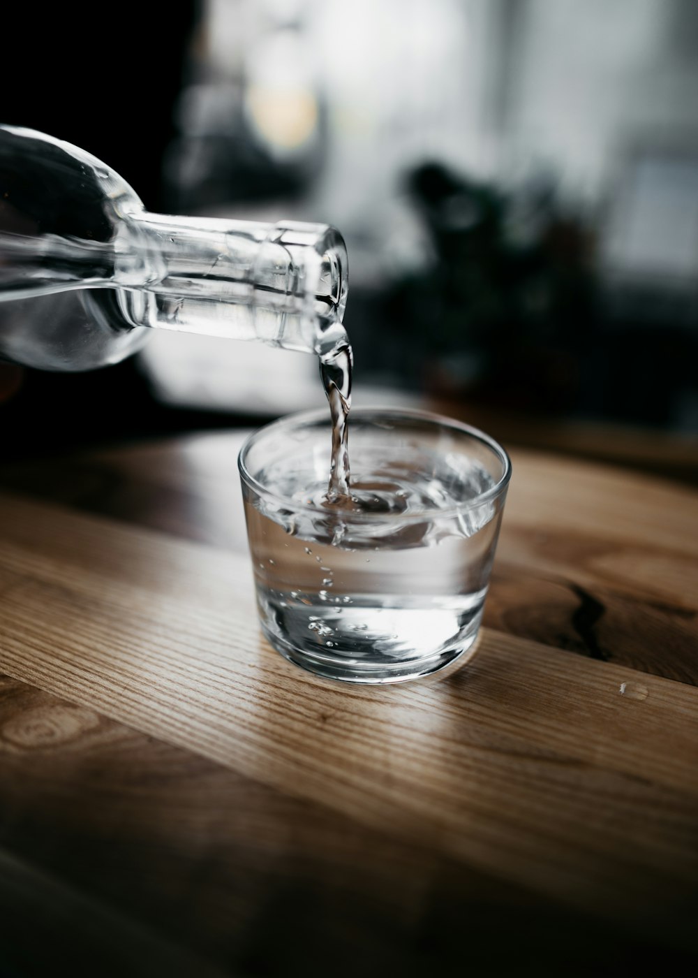 Person mit Flasche gießt Wasser auf Trinkglas
