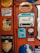 A variety of vintage advertisement signs and labels are affixed to a red wall. These include ads for products such as soap, milk, kerosene, and a radio. The designs are colorful and nostalgic, featuring retro typography and illustrations.
