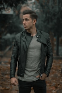 A man wearing a sleek, casual black jacket standing outdoors in autumn leaves