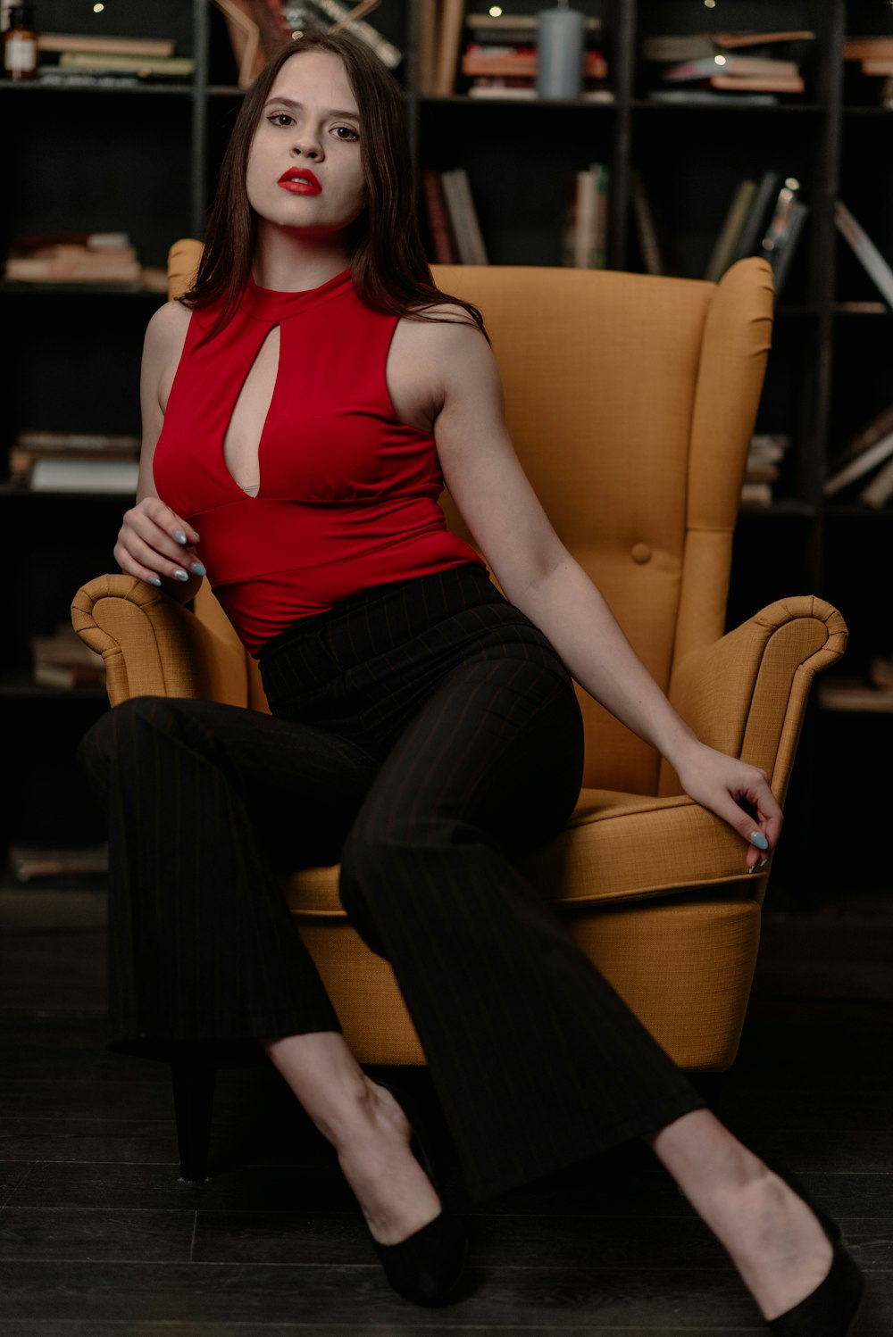 woman wearing red sleeveless top sitting on brown wingback chair