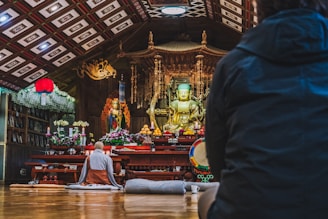 Monks and visitors sitting peacefully in a serene meditation hall surrounded by lotus flowers.