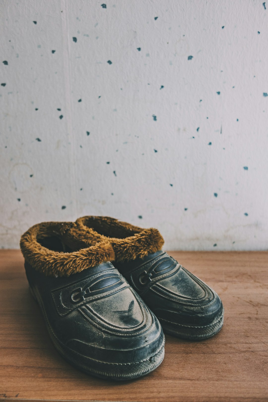 pair of black-and-brown leather fleece shoes beside white wall