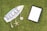A surfboard-shaped sign with the words 'Relax, Life is Good' printed on it is placed on grass. Attached to the sign are a starfish and a seashell. Nearby is an empty black picture frame with a white space inside.